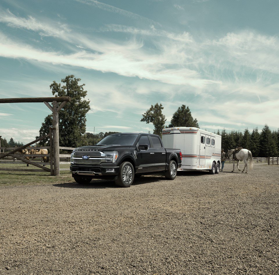 2026 Ford F-150® Platinum® pickup in Agate Black hitched to a horse trailer parked near a ranch
