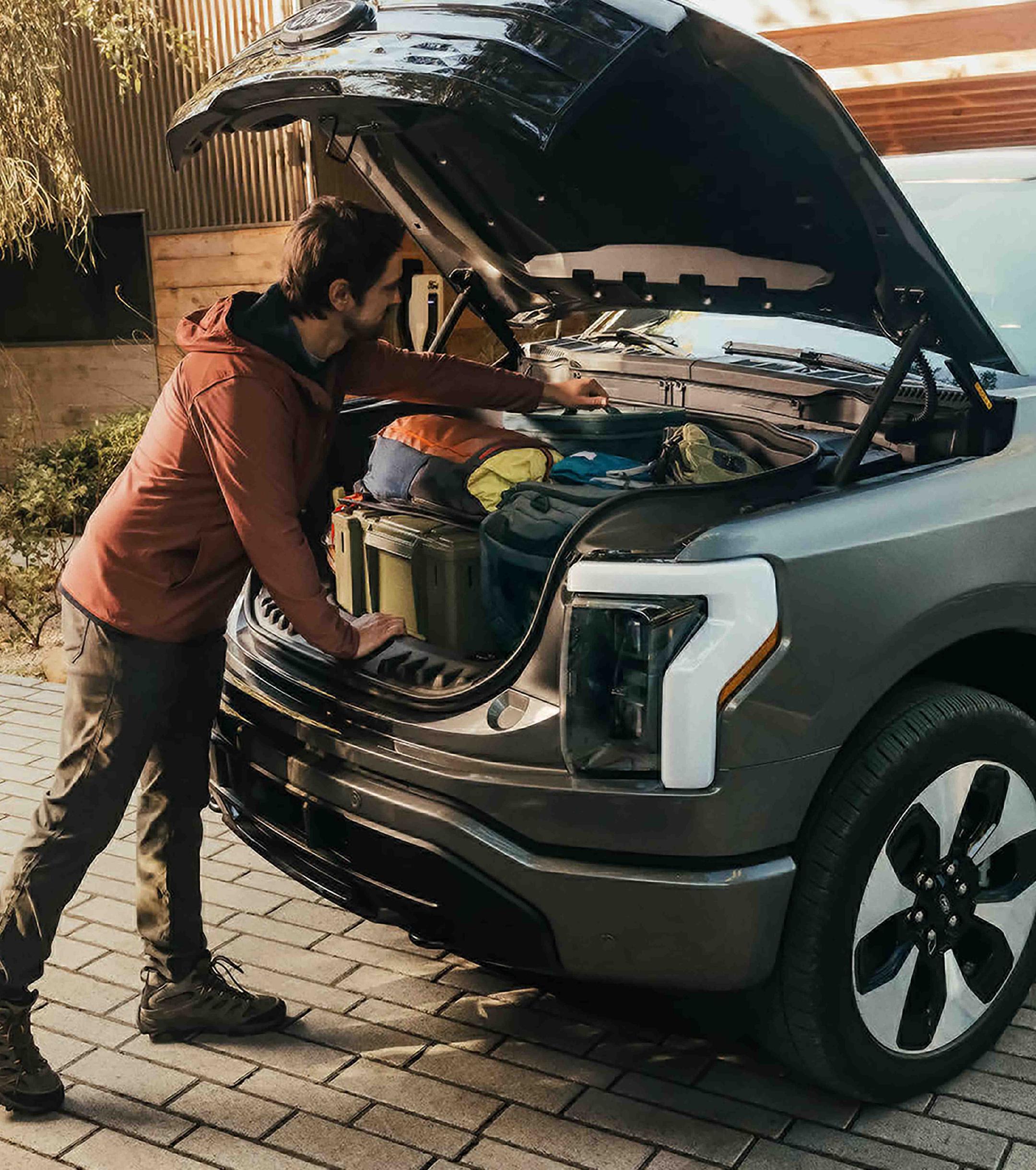 A man reaching into the Mega Power Frunk on a 2025 Ford F-150 Lightning® pickup, which is filled with boxes and bags
