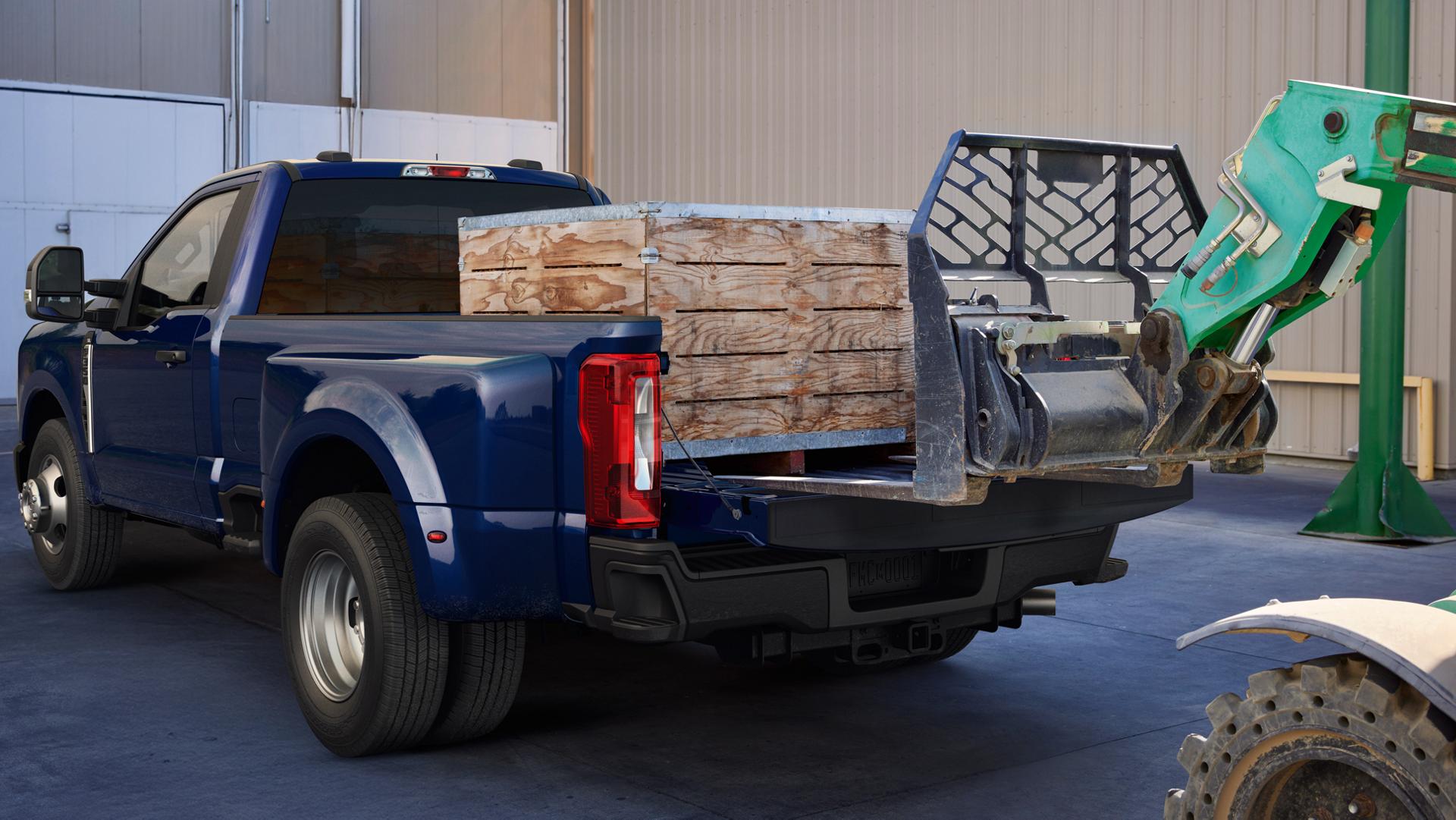 A 2026 Ford Super Duty® F-350® Lariat® model in Argon Blue with a heavy crate being loaded into the truck bed