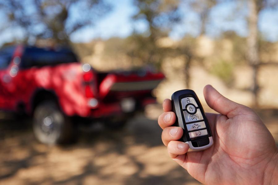 Hand holding key fob with red 2025 Ford Super Duty® King Ranch® pickup in the background