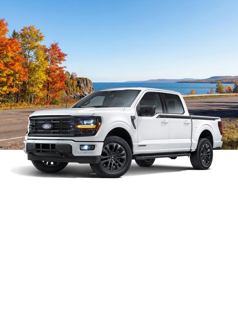 White Ford F-150® truck with the Great Lakes Package, with a calm blue water and evergreen tree-lined shoreline background