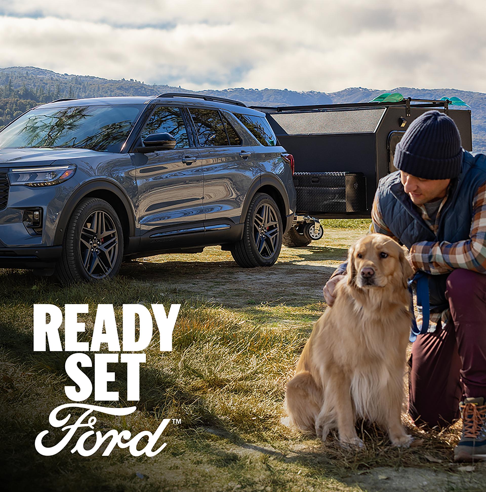 A 2026 Ford Explorer® parked outside towing a camper with a man and dog in the foreground
