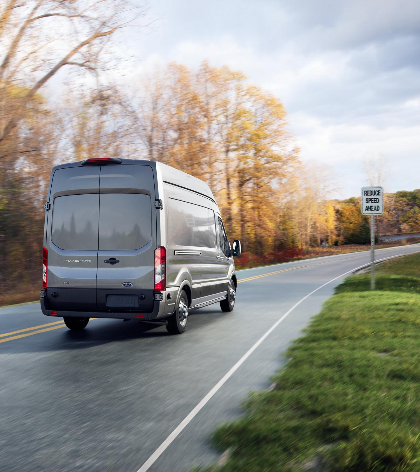 Rear shot of a 2025 Ford Transit® van being driven down a road with speed limit sign