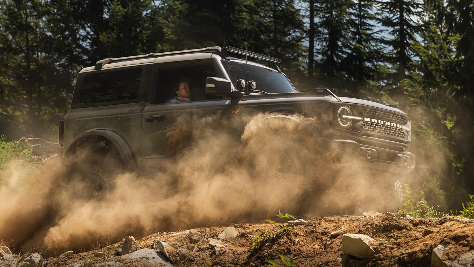 A green 2026 Ford Bronco Badlands two-door driving on a rocky trail. 