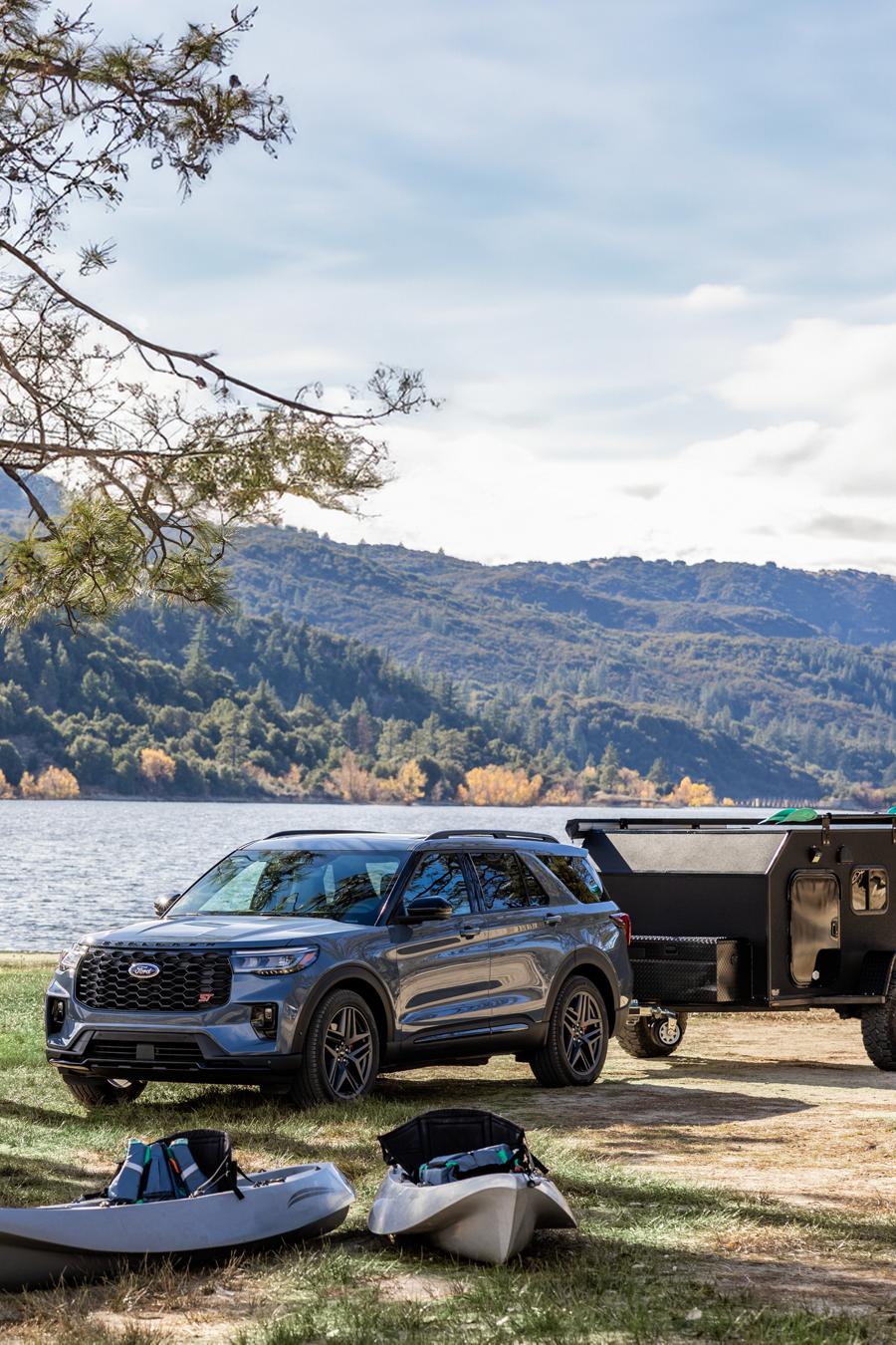 A 2025 Ford Explorer® SUV with a trailer parked near the edge of a lake with a family setting up a tent at their camp site
