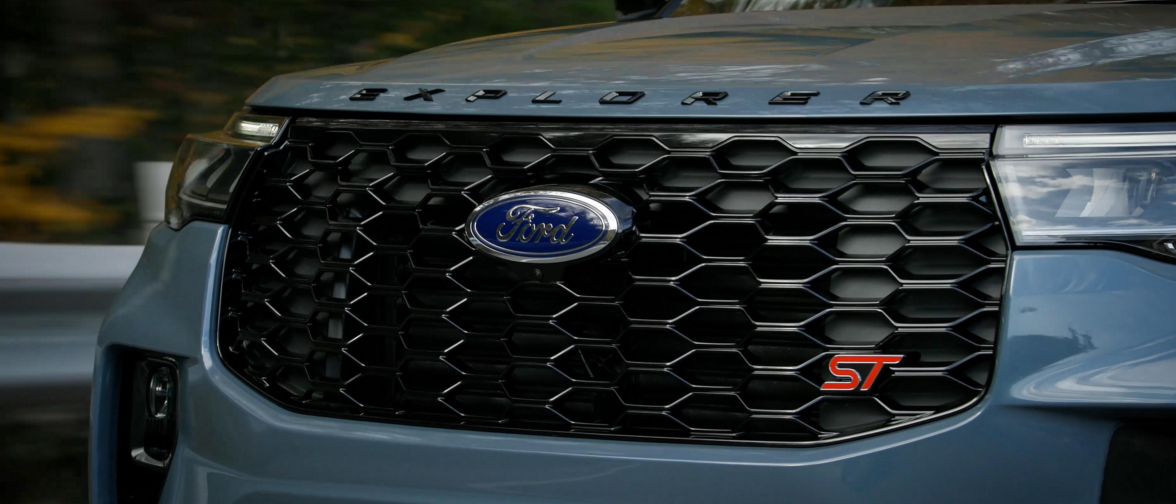 A 2025 Ford Explorer ST in Vapour Blue Metallic driving on a dirt road through a hilly and forested terrain