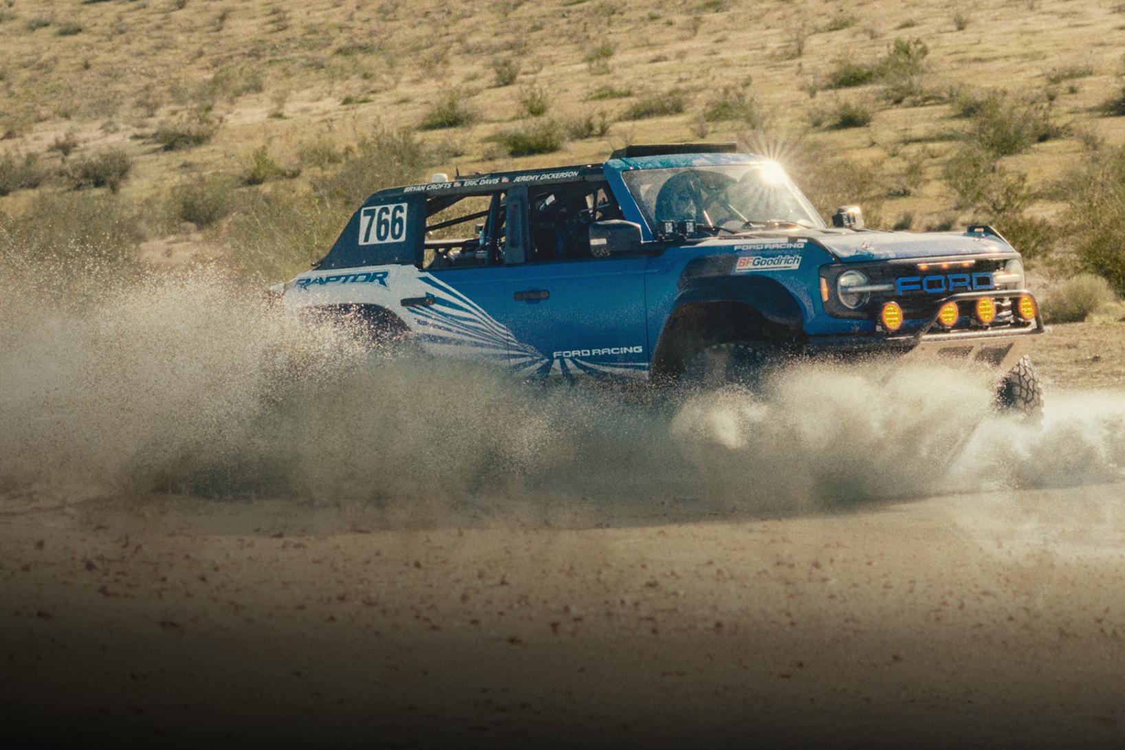 A blue with white graphics 2025 Ford Bronco® Raptor® racing through the desert