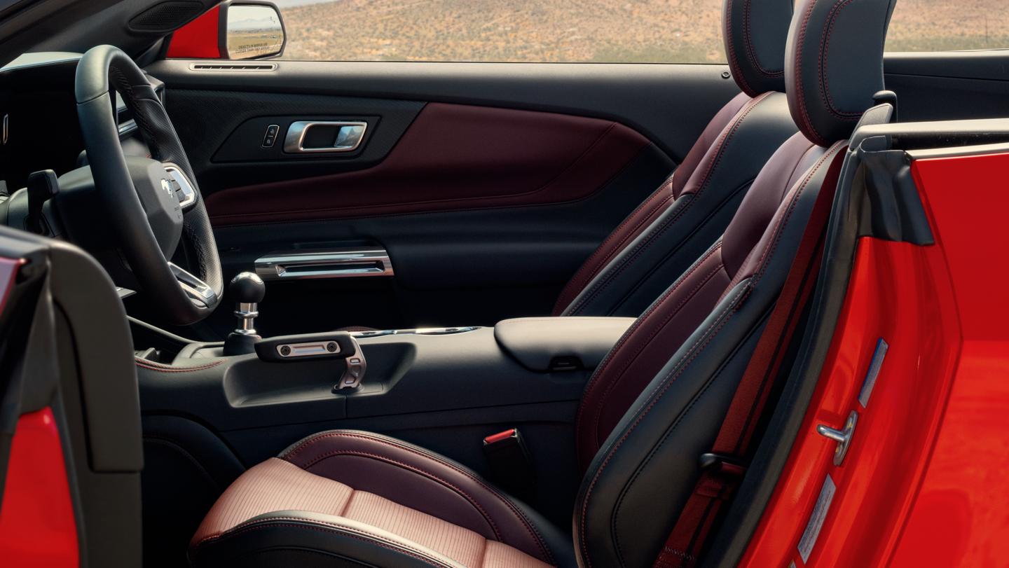 Parked 2025 Mustang® convertible with the driver's side door open showing the available Carmine Red interior