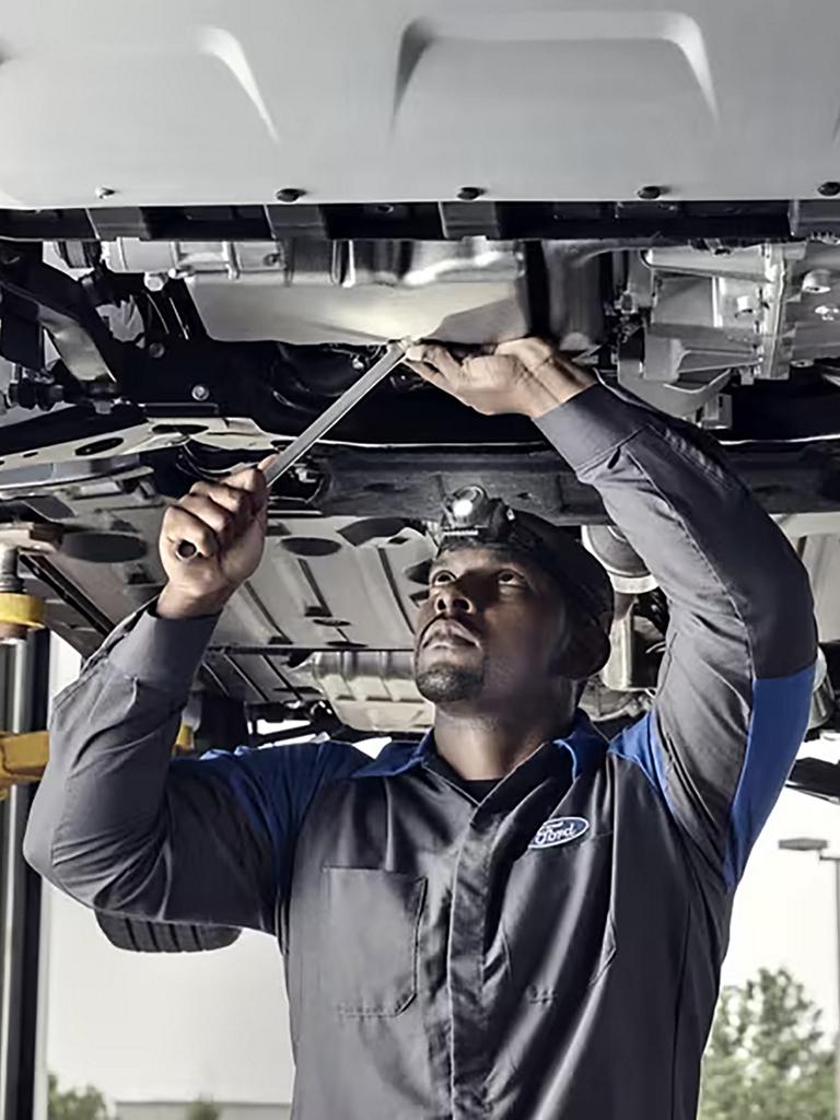 A Ford service technician works on the underside of a vehicle