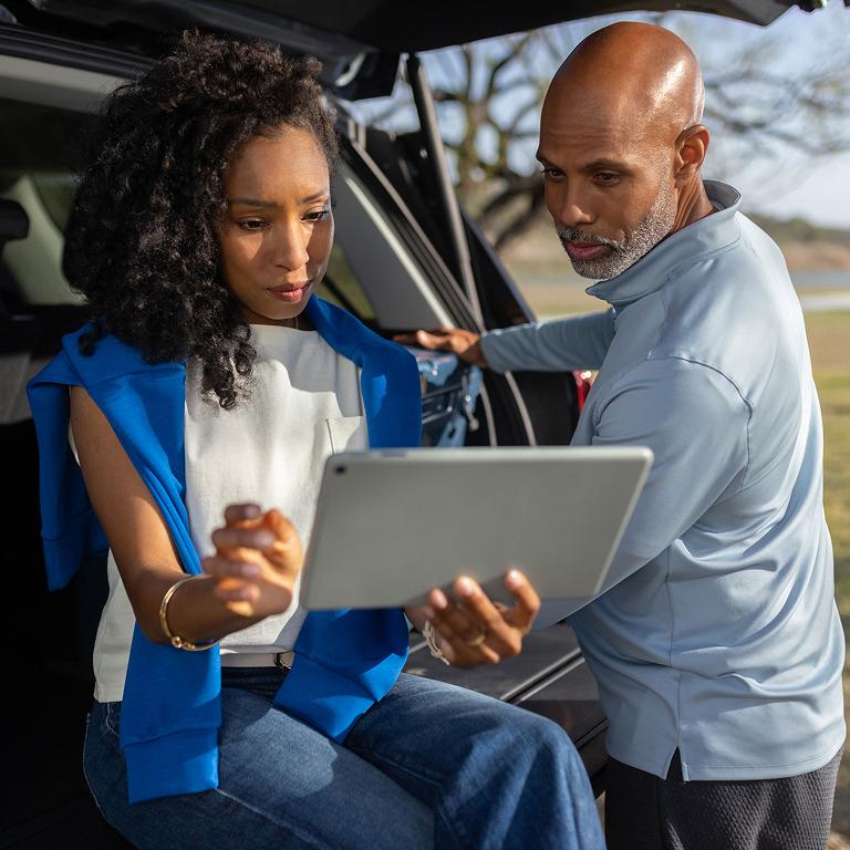 Family members in a parked vehicle using a laptop and mobile device.