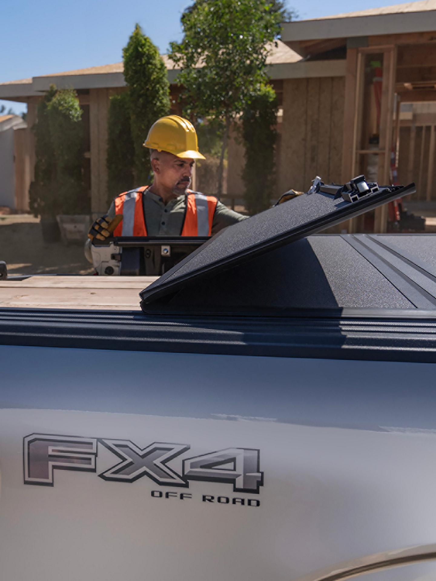 Construction worker opens the folding bed cover on a Ford F-150 Lightning®