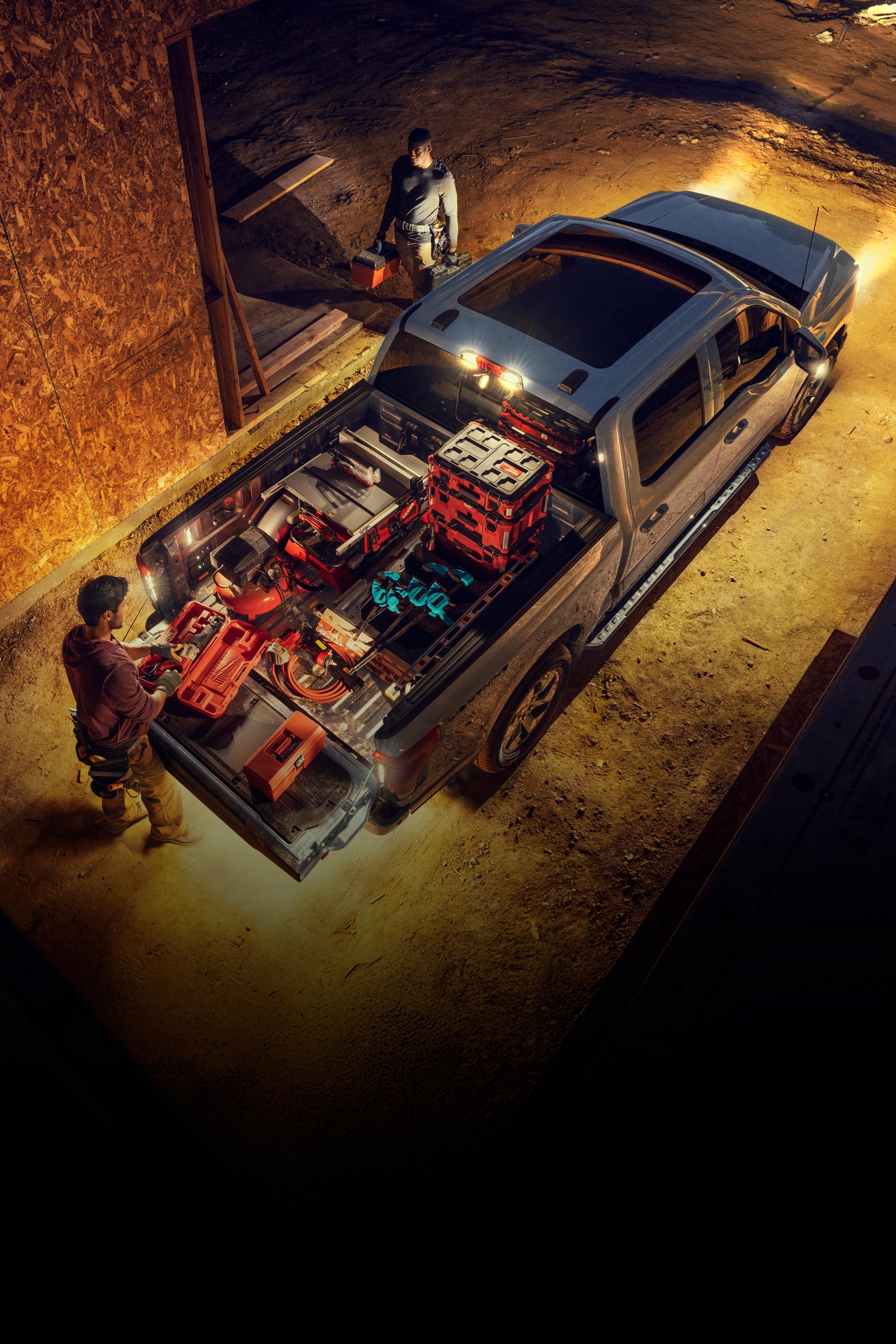 An overhead shot of a 2025 Ford F-150® Lightning® truck parked with a man grabbing tools from the truck bed at night