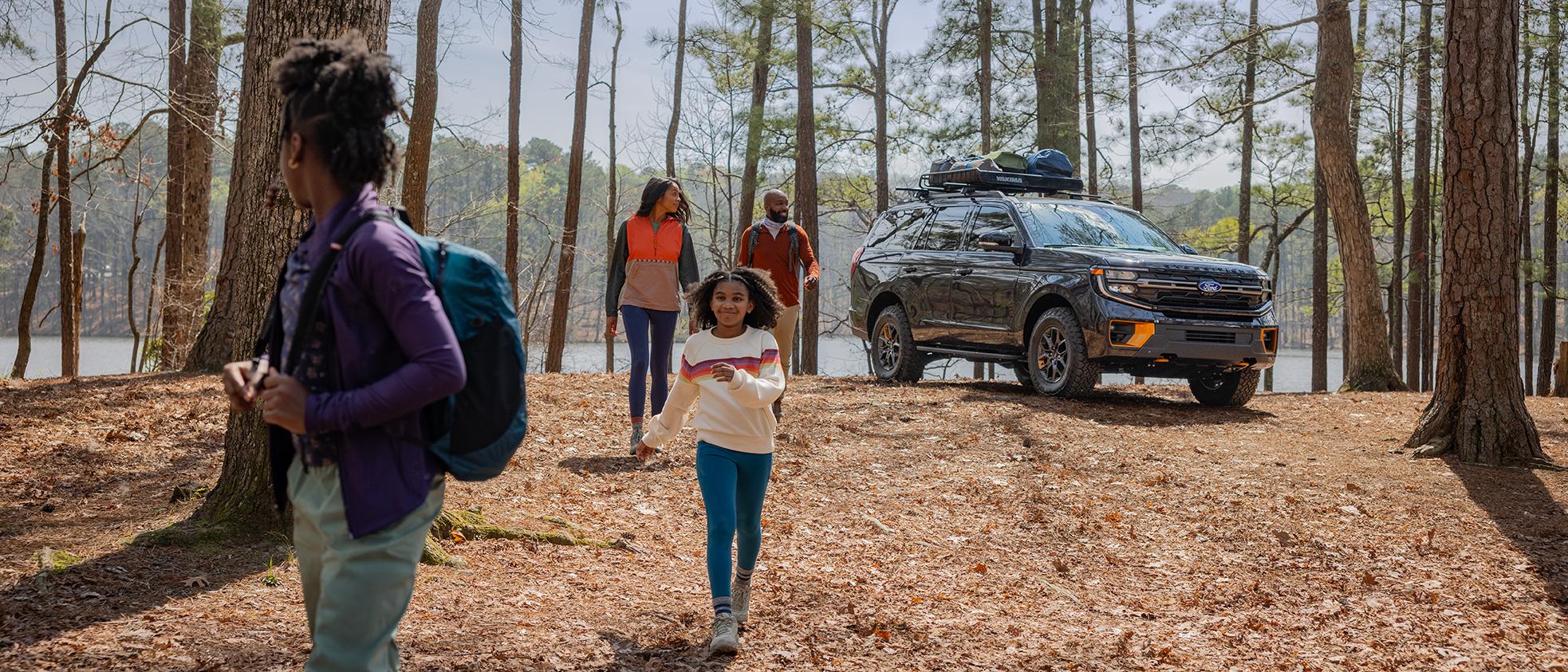 Family of four in the woods with a 2026 Ford Explorer® SUV parked behind them