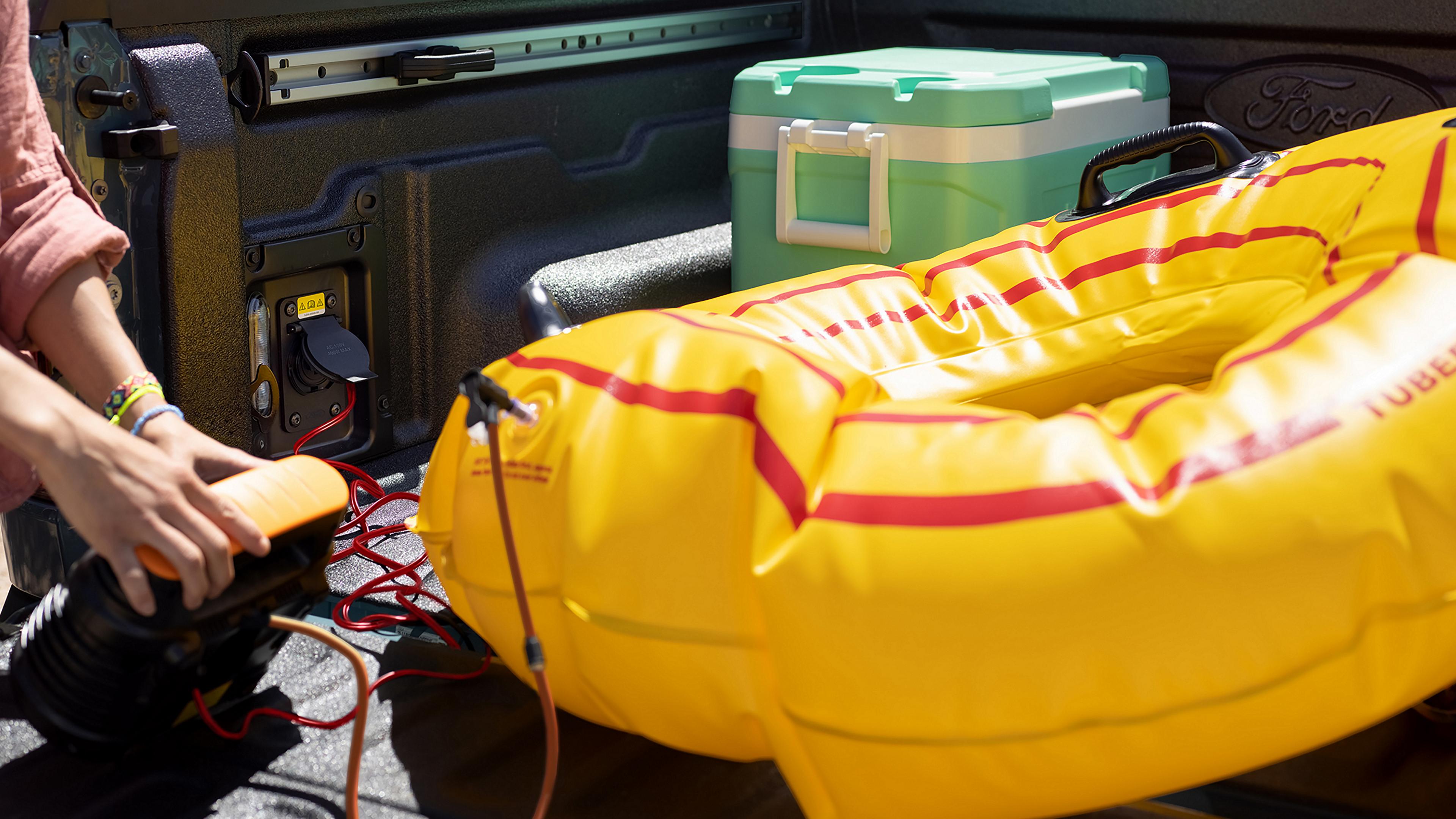 A person using built-in outlet in the cargo bed of a 2026 Ford Maverick® pickup to power an air pump to inflate a raft