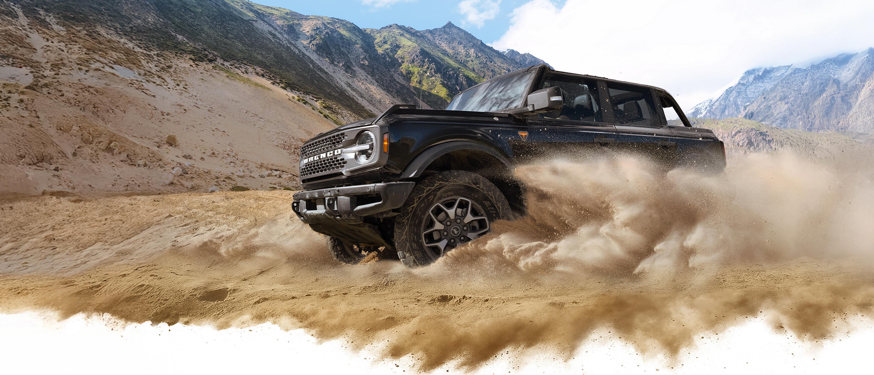 A 2026 Ford Bronco® SUV kicking up dust in a valley beneath rocky hills
