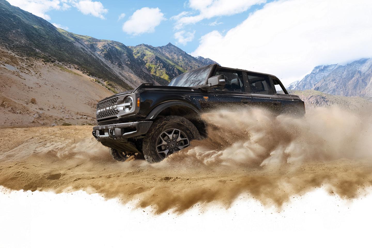 A 2026 Ford Bronco® SUV kicking up dust in a valley beneath rocky hills