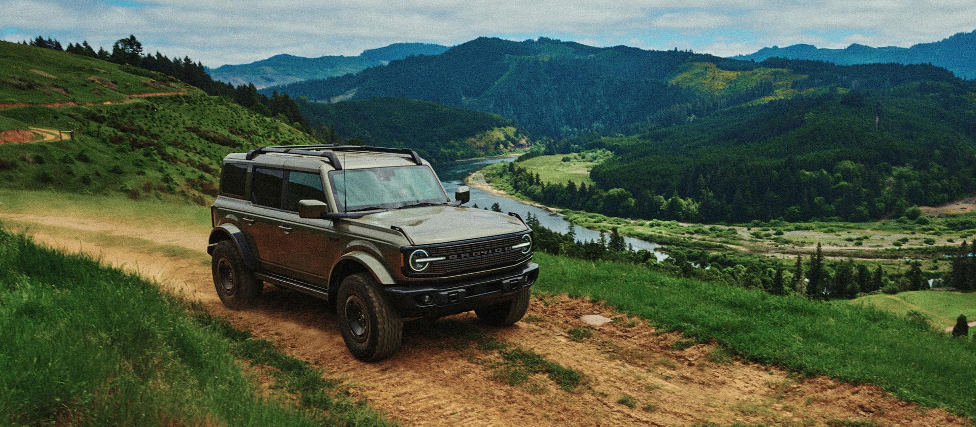 2027 Ford Bronco® Filson SUV being driven on a dirt track along the crest of a hill, overlooking a river valley