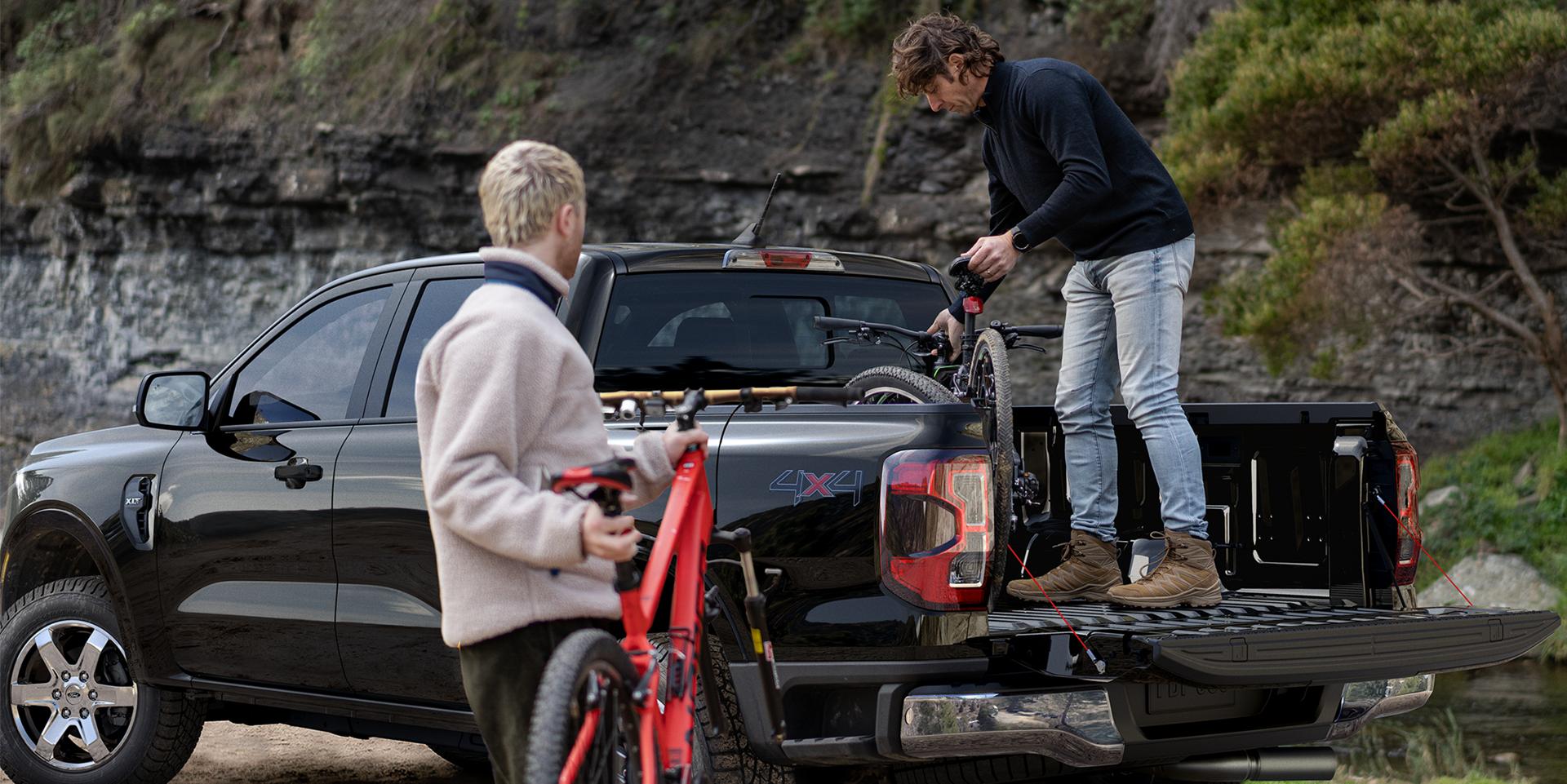 Two men loading bicycles into a black Ford Ranger’s truck bed.
