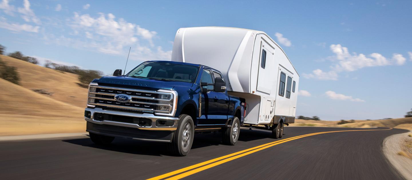 2025 Ford Super Duty® XLT model in Antimatter Blue pulling a large camper on a paved roadway