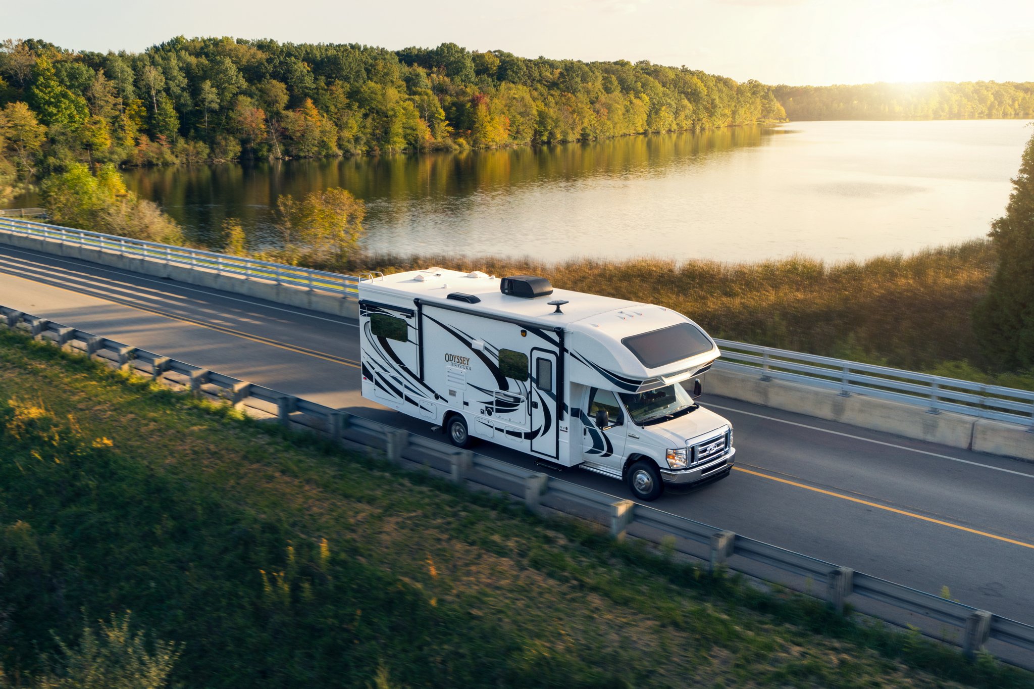 Fourgon tronqué à roues arrière jumelées Ford série E 2025 avec autocaravane de classe C circulant près d’un grand plan d’eau