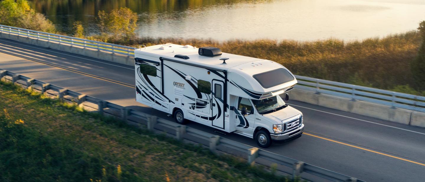 Fourgon tronqué Ford série E 2025 avec autocaravane de classe C circulant près d’un grand plan d’eau