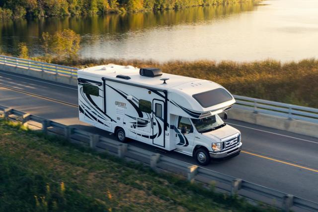 Fourgon tronqué Ford série E 2025 avec autocaravane de classe C circulant près d’un grand plan d’eau