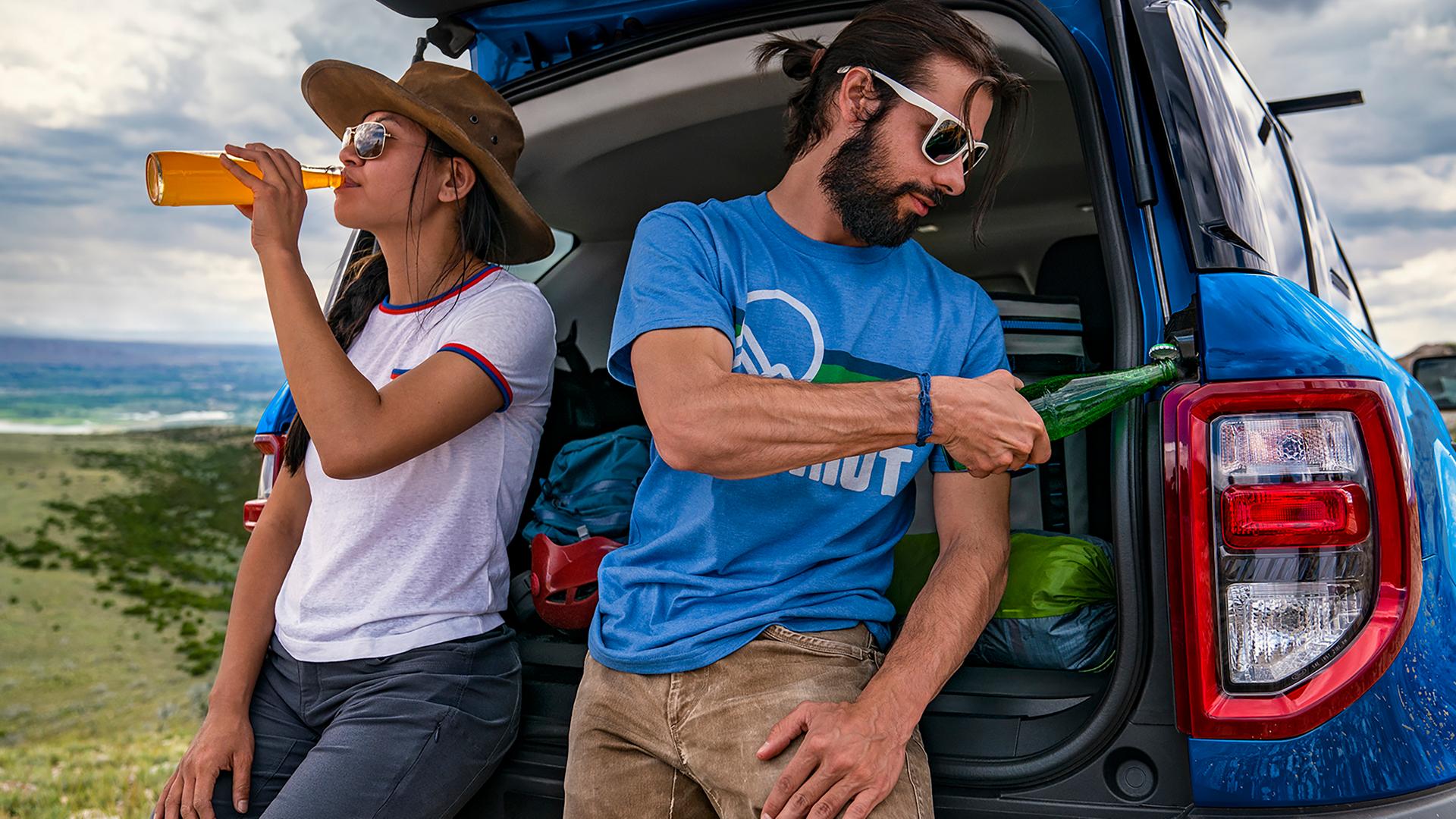 Two people leaning against the tailgate and using the built-in bottle opener
