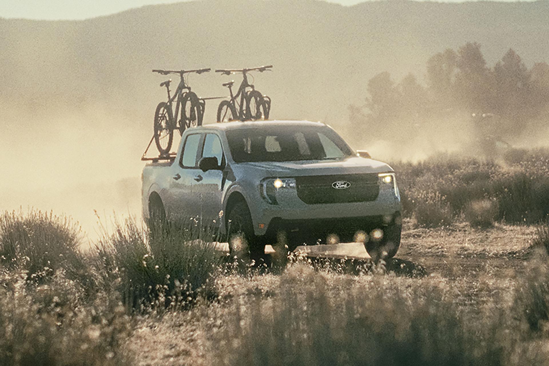 A 2025 Ford Maverick® pickup with bicycles in the truck bed is being driven on a dusty trail