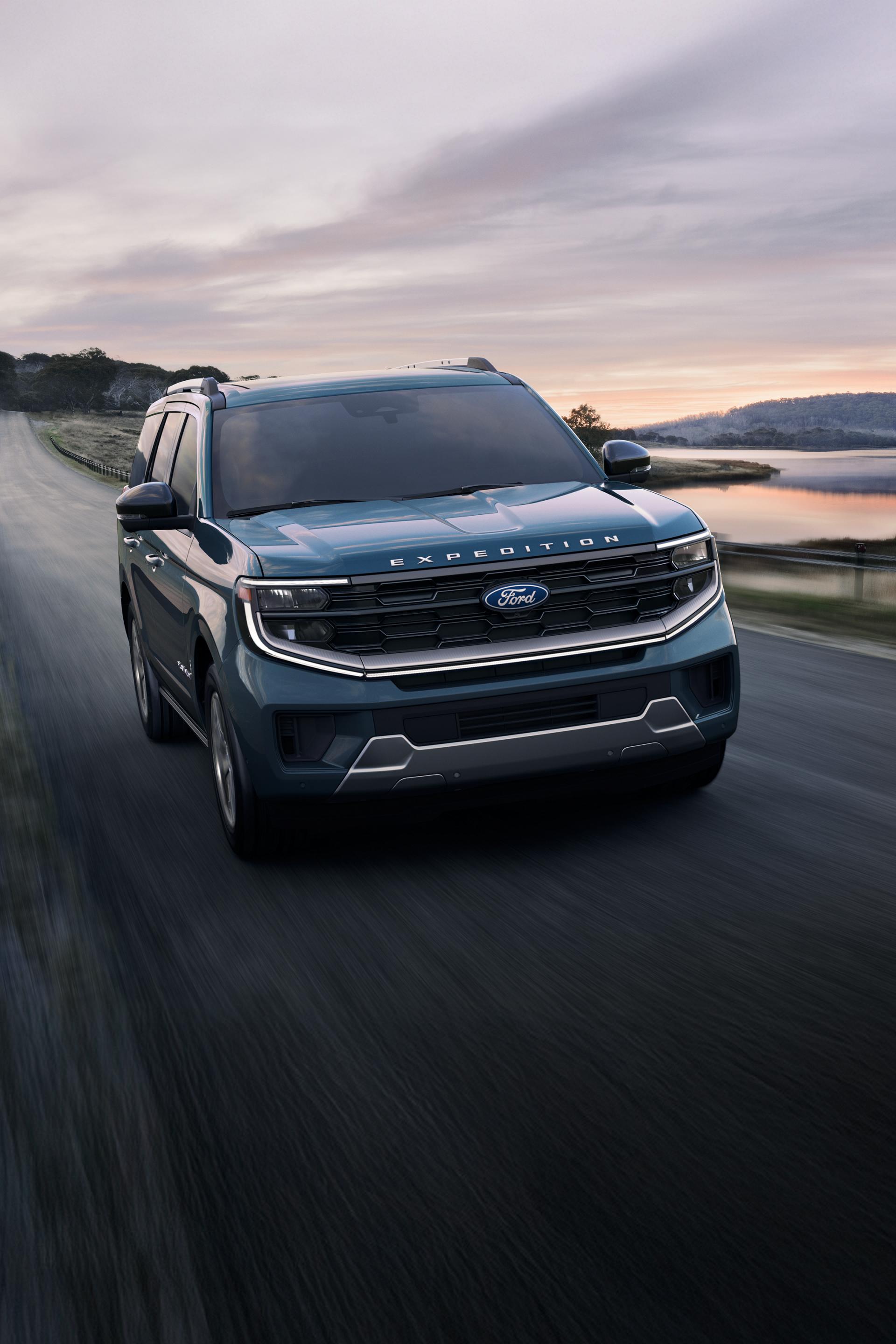 A blue 2025 Ford Expedition driving on a paved road next to a lake