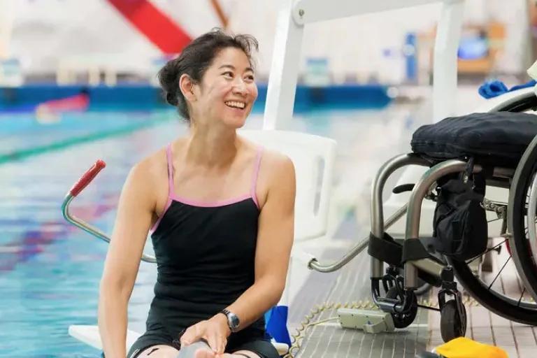Woman sitting on the edge of a pool with wheelchair in background