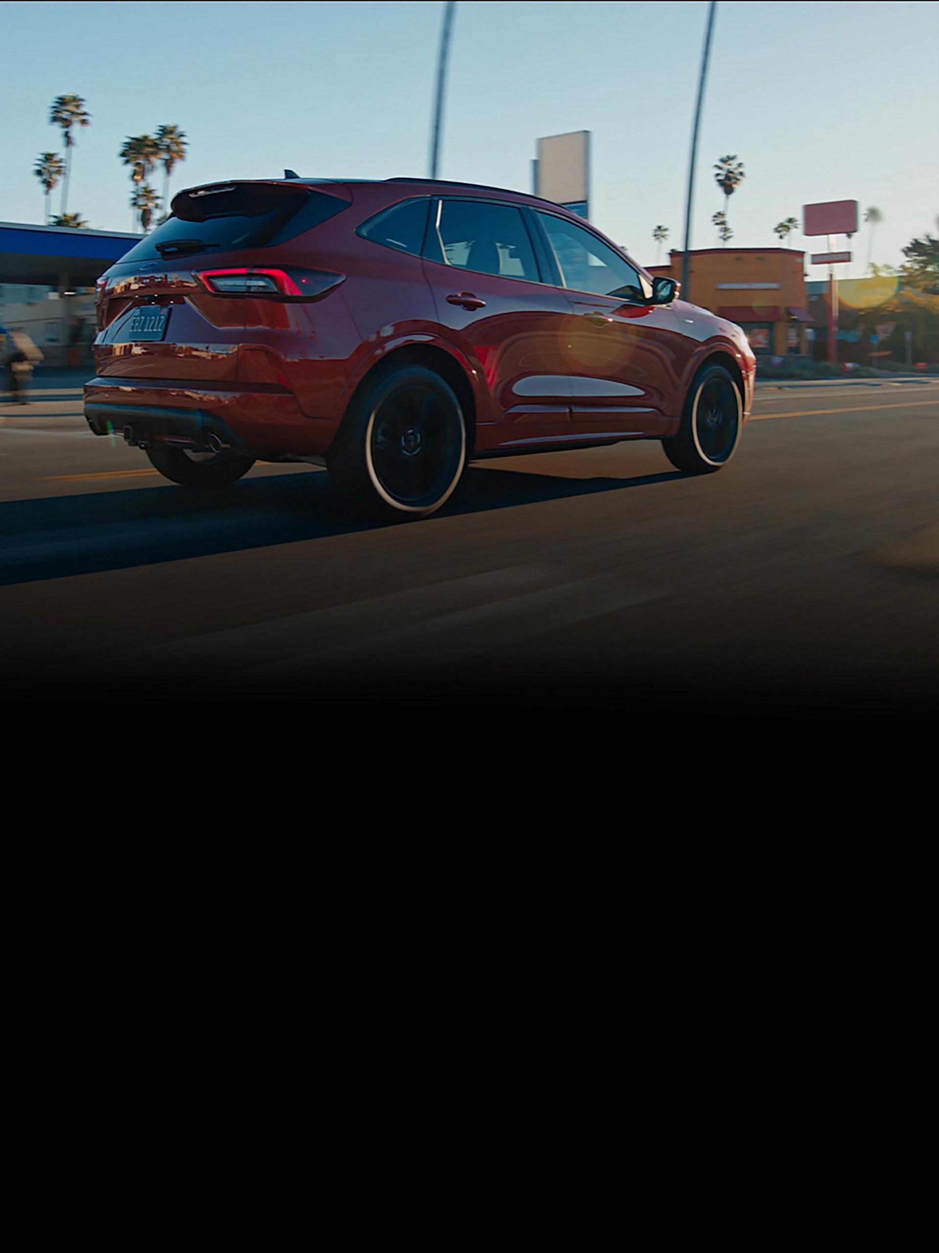 A 2026 Ford Escape® SUV being driven at sunset along a city street dotted with palm trees