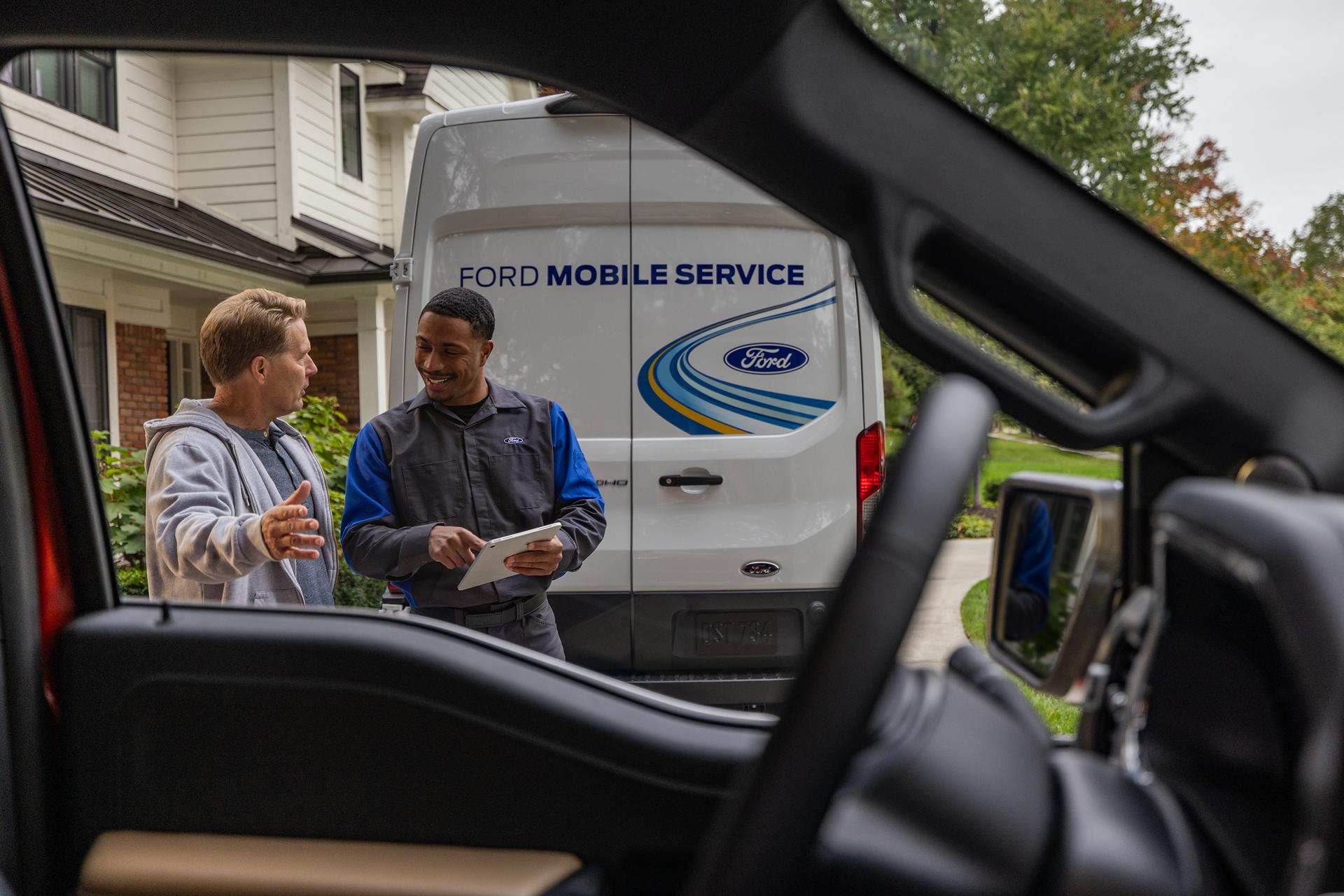 A Ford service tech talks to a customer while standing in front of a Ford Mobile Service van