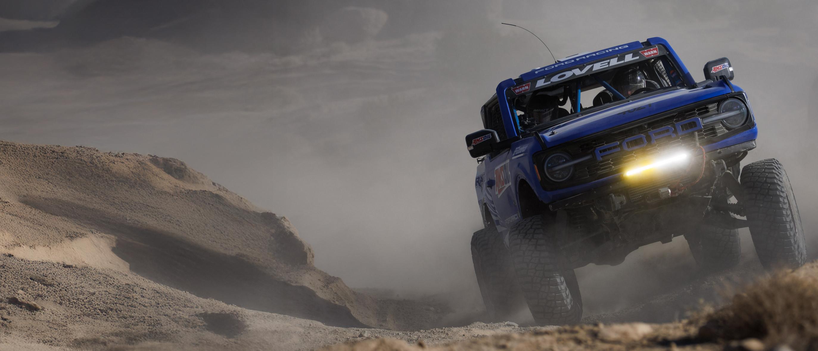 A blue 2025 Ford Bronco Raptor racing on dirt terrain