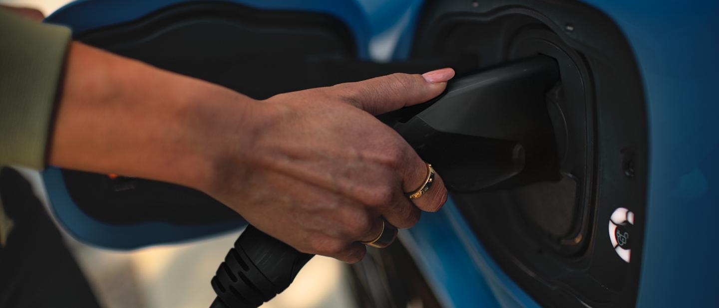 A woman’s hand seen plugging in a 2023 Ford Mustang Mach-E® to charge