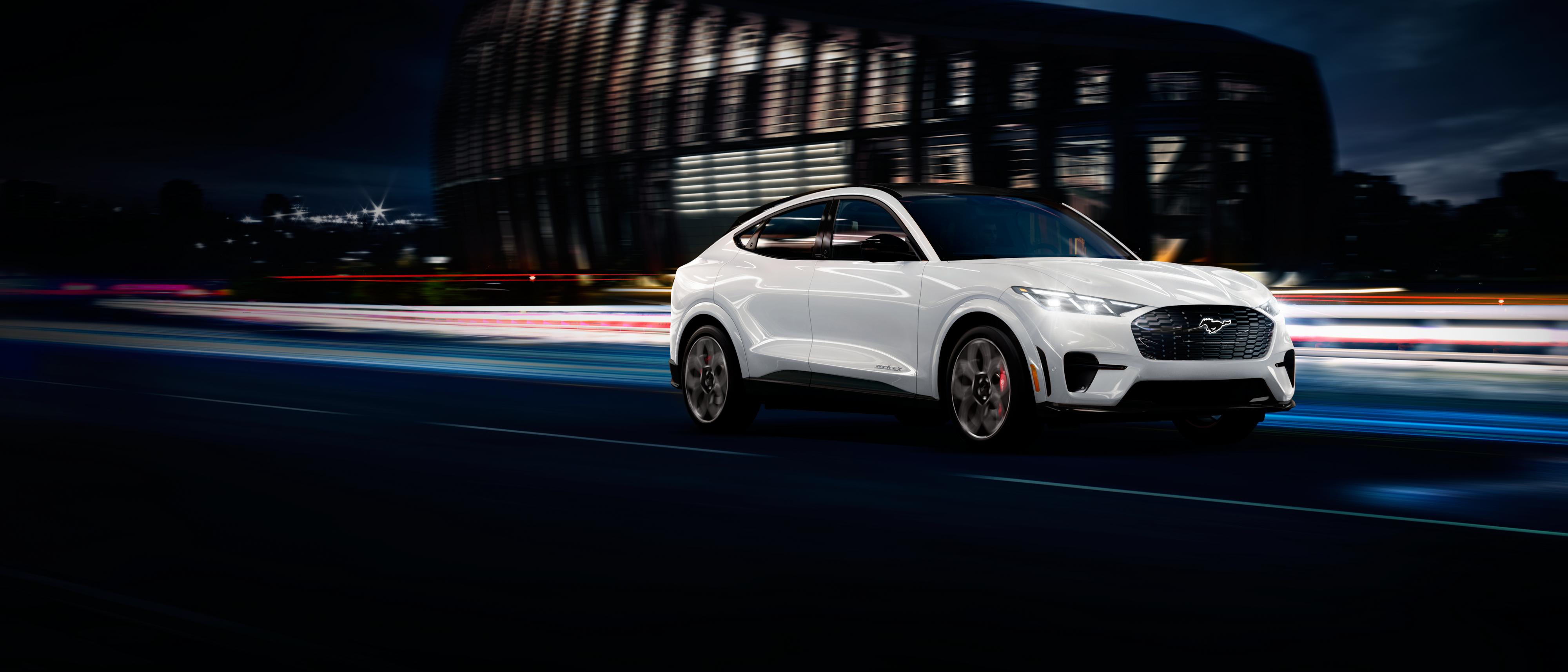 A white Ford Mustang Mach-E speeds down a highway at night.