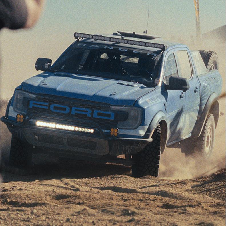 A blue with white graphics 2025 Ford F-150® Raptor® racing through the desert