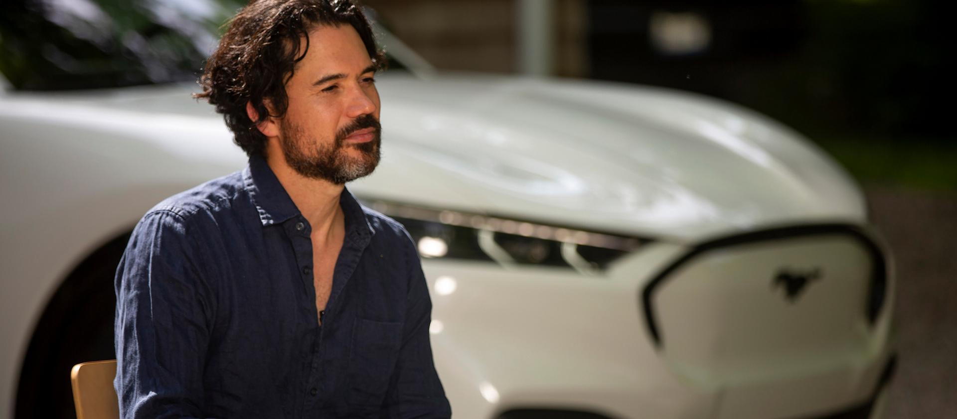 A man sitting on a chair in front of a Ford Mustang Mach-E