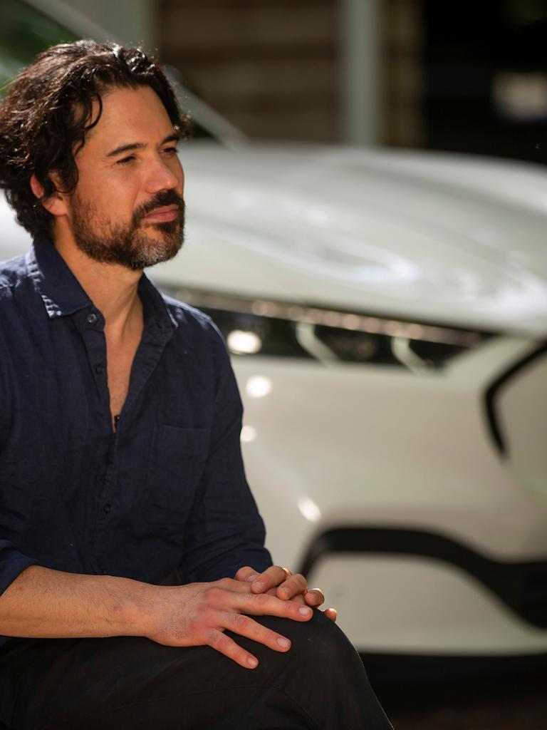 A man sitting on a chair in front of a Ford Mustang Mach-E