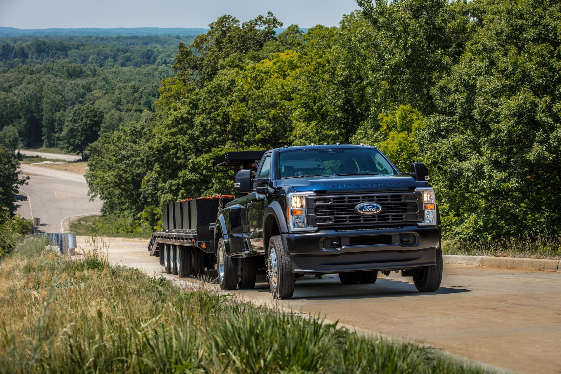 A 2024 Ford Super Duty® Regular Cab in Antimatter Blue Metallic tows a flatbed trailer on a dirt road