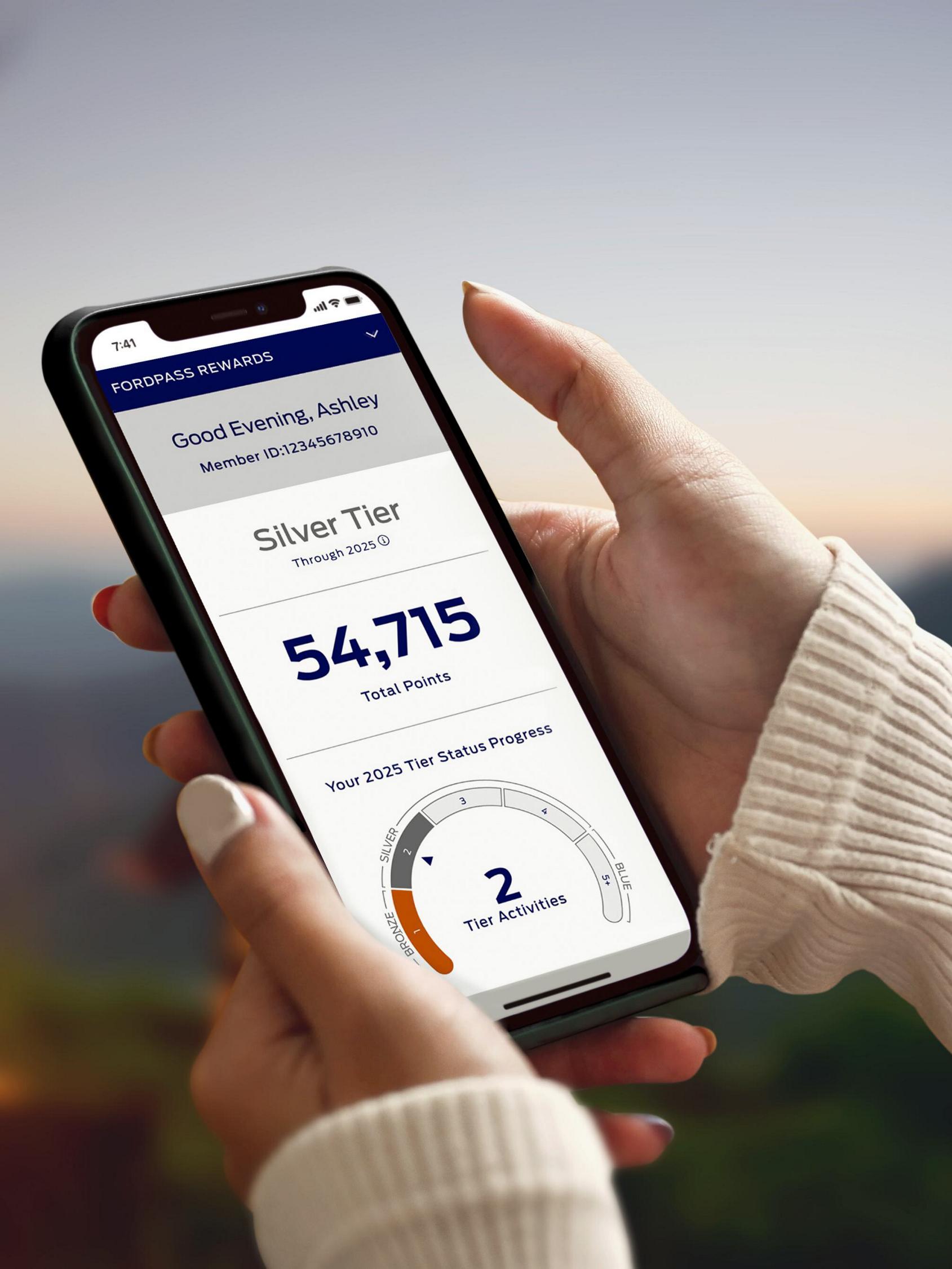 Hands are holding a smartphone and interacting with the Ford Rewards dashboard
