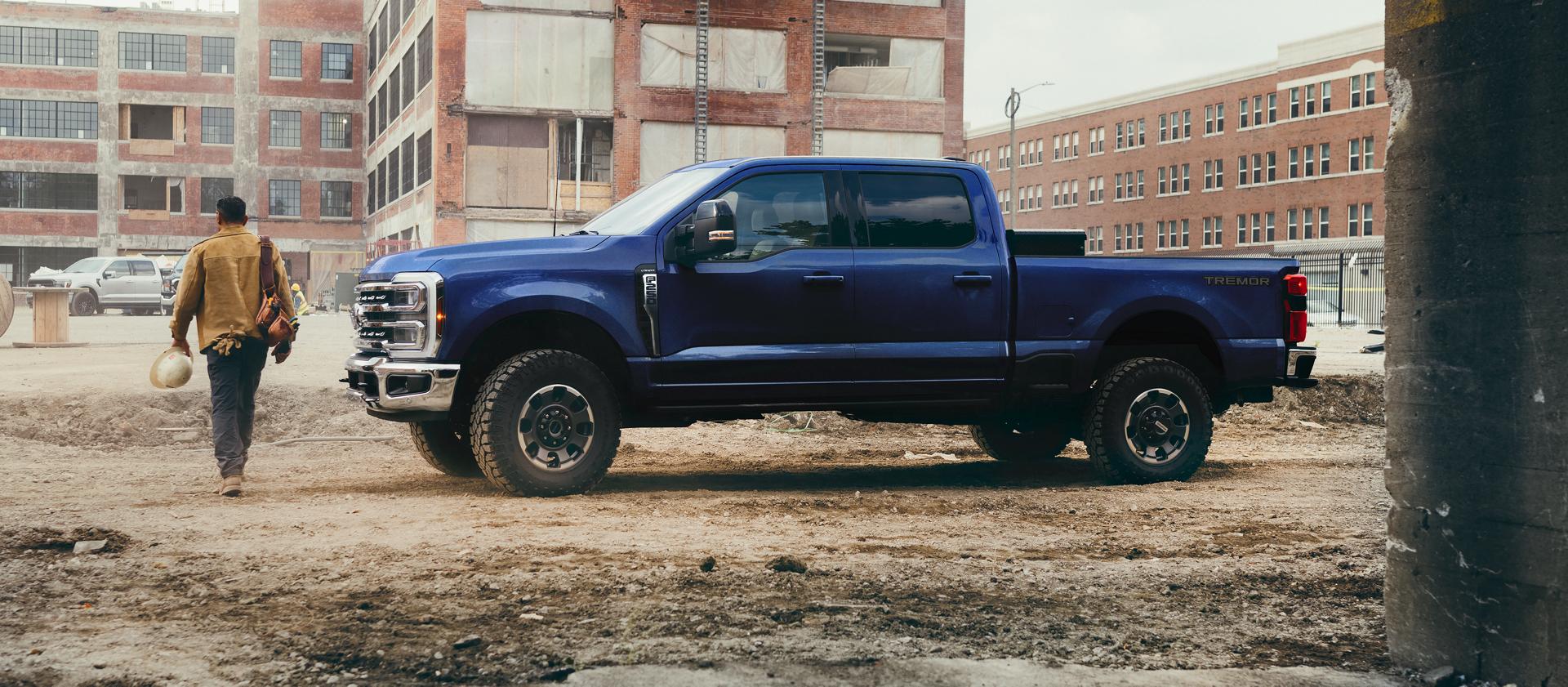 A person walking away from their 2026 Ford Super Duty® F-250® Lariat® pickup in Argon Blue on a construction site
