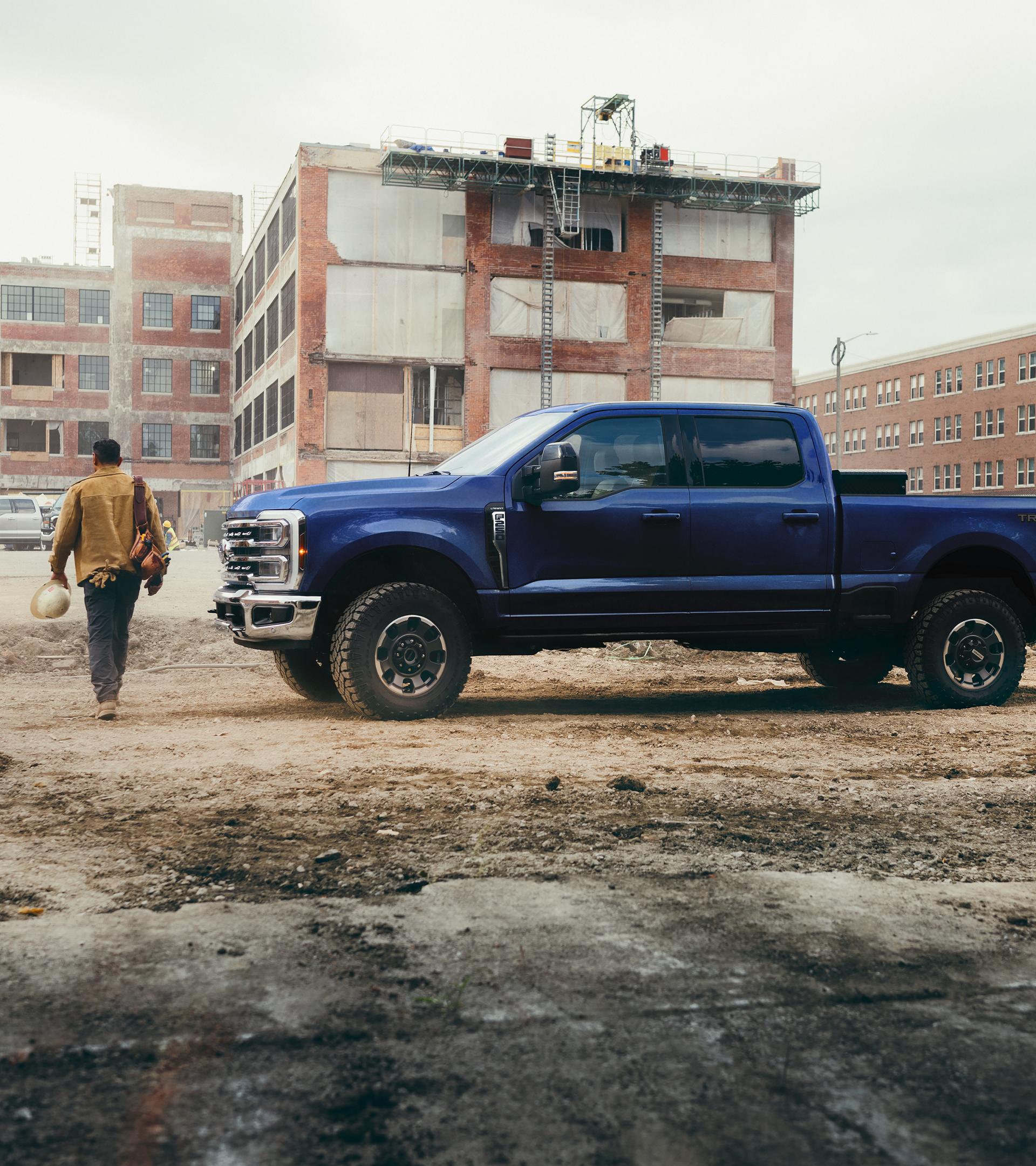 A person walking away from their 2026 Ford Super Duty® F-250® Lariat pickup in Argon Blue on a construction site