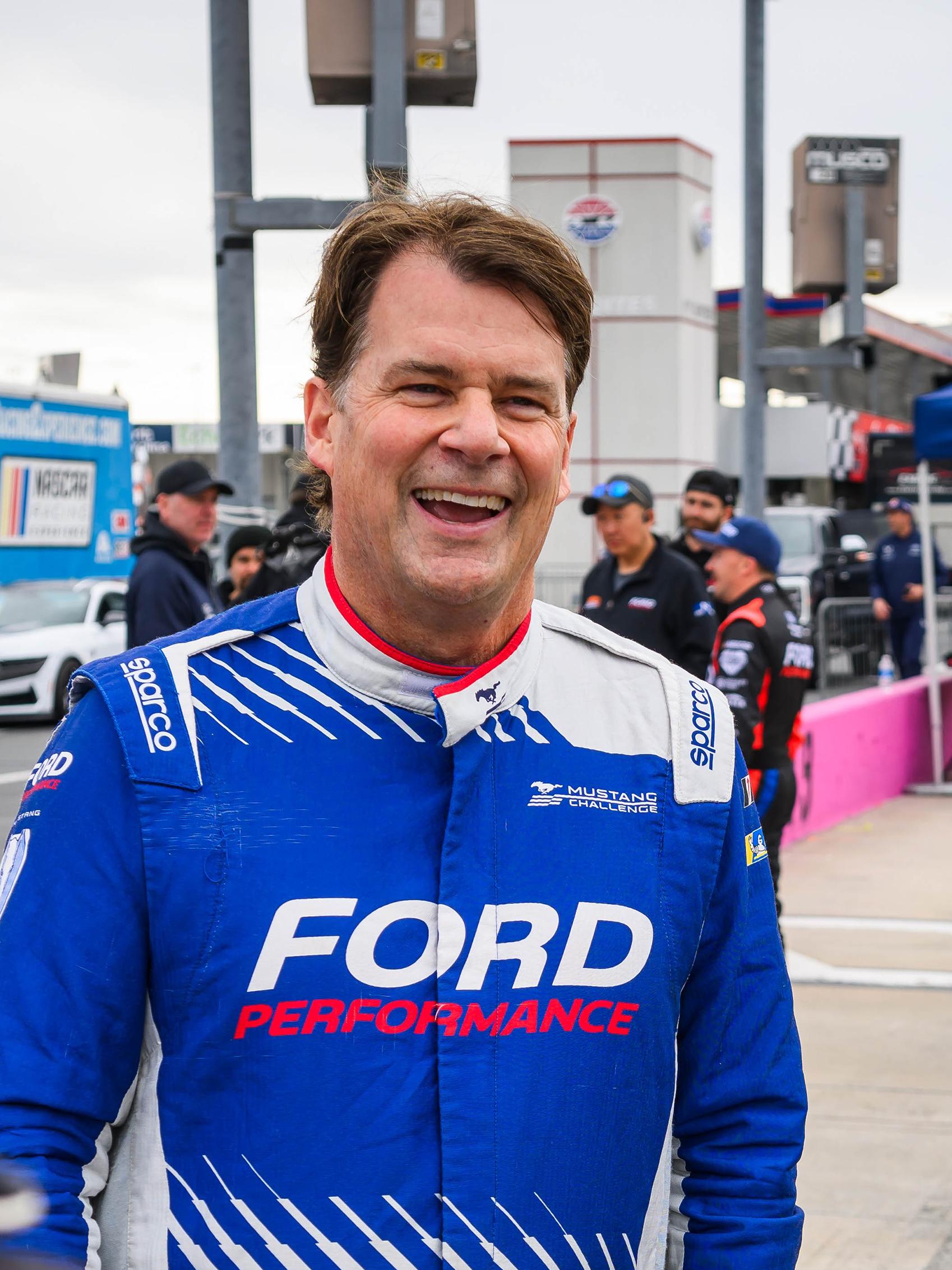 Jim Farley in a Ford Performance track suit smiles at a race track
