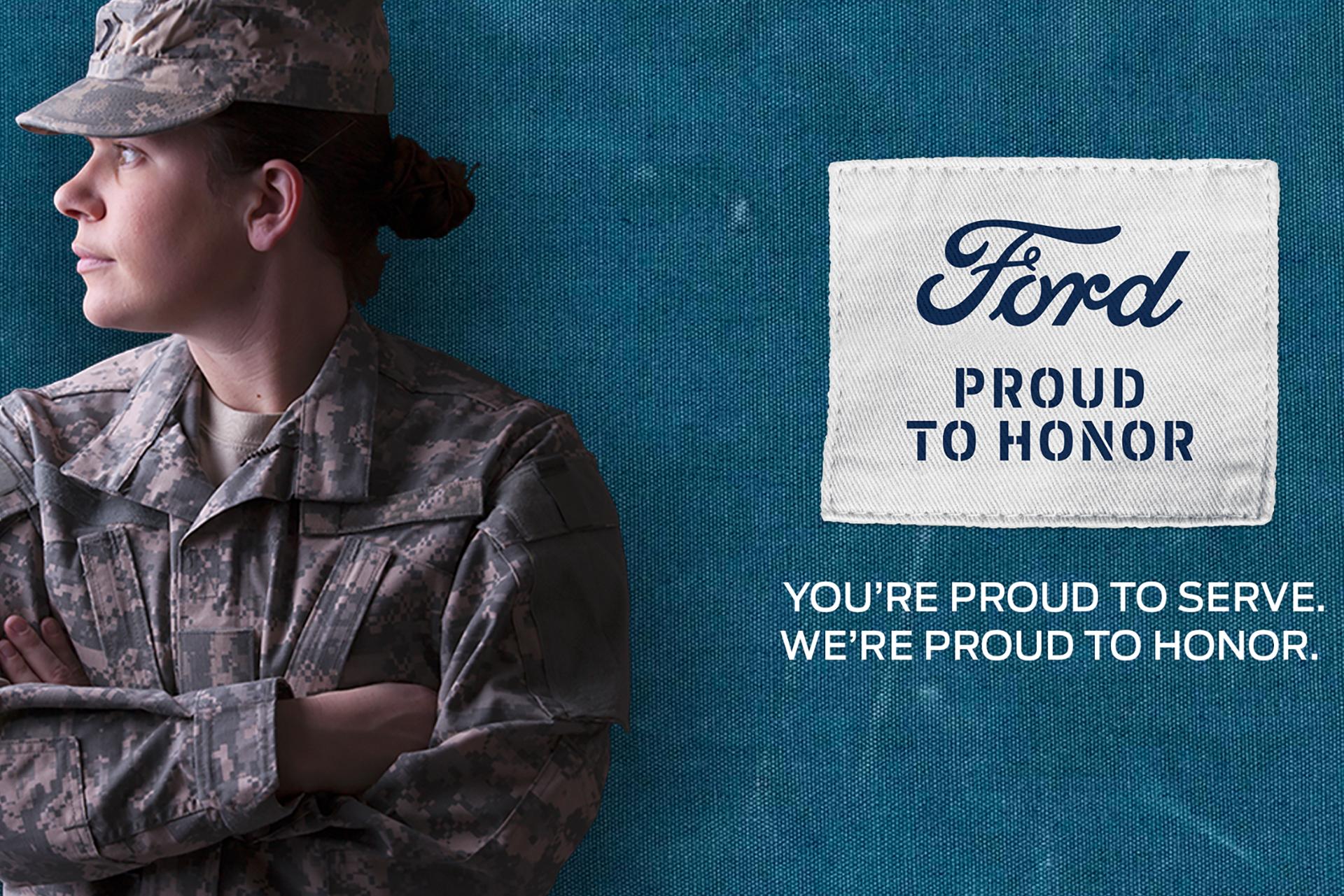 A service member in military fatigues stands arms crossed next to a Ford Proud To Honor Logo