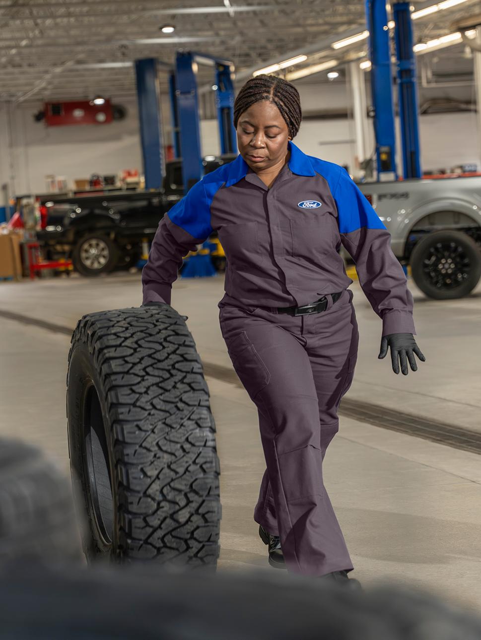 A Ford Service technician rolls a new tire toward a vehicle