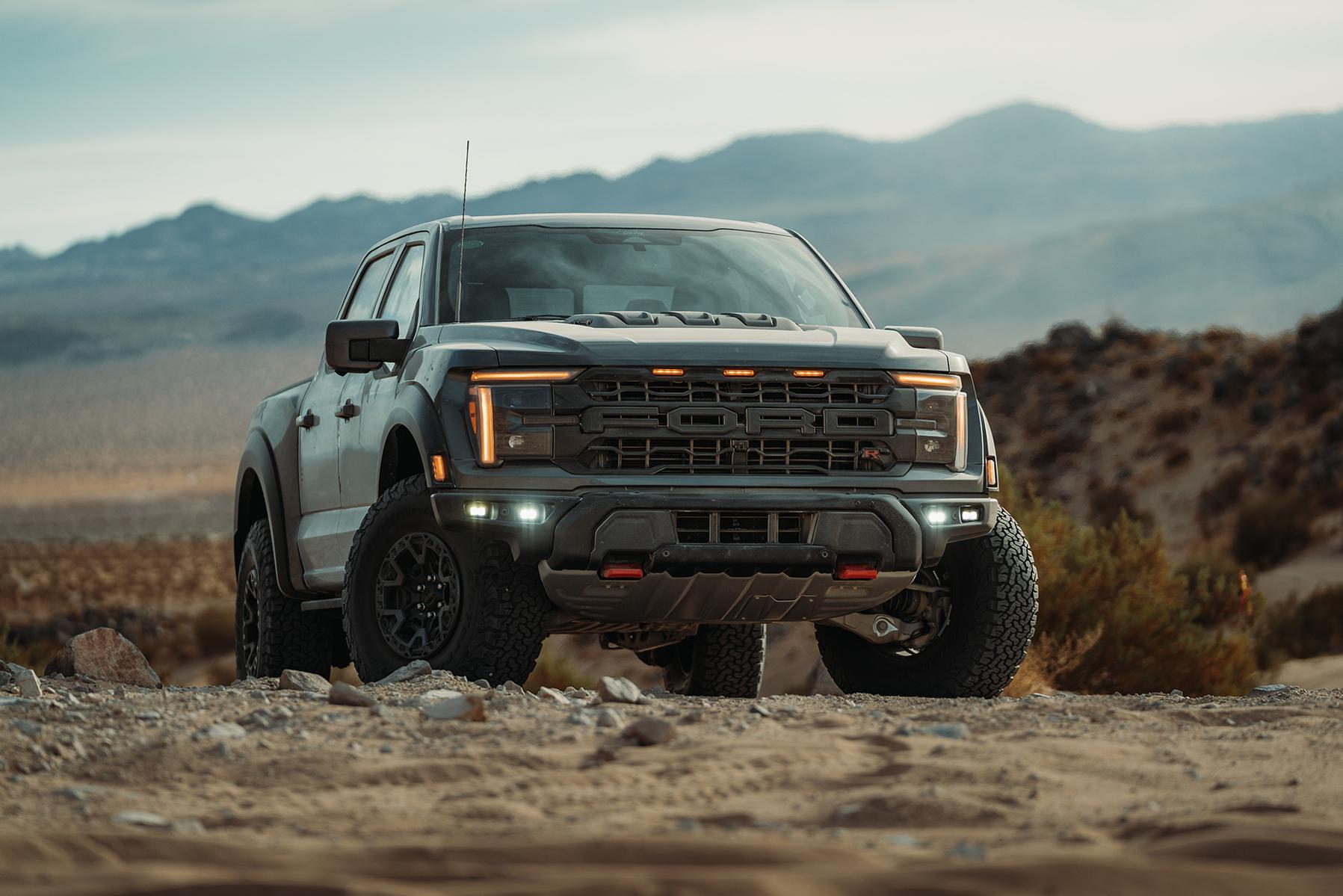 A head-on close-up of a distinctive 2024 Ford F-150 Raptor® front grille, featuring the bold, black 'FORD' block lettering