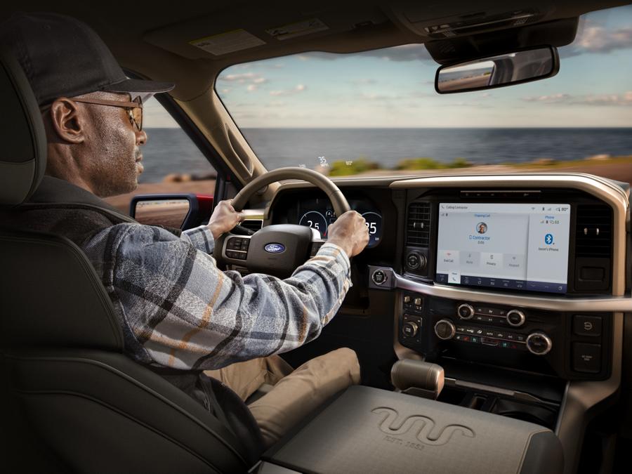 A man driving a Ford F-150 pickup truck uses the Amazon Alexa virtual assistant to make a phone call. Information about the call is displayed on the vehicle's SYNC touchscreen.