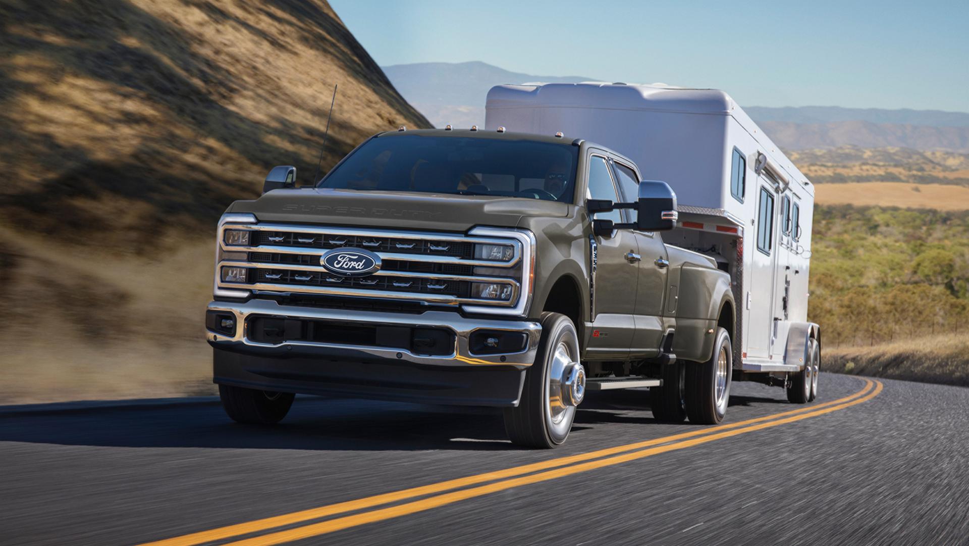 2026 Super Duty® F-350® Lariat® model with the Chrome Package driving on a hilly paved road while towing a large trailer.