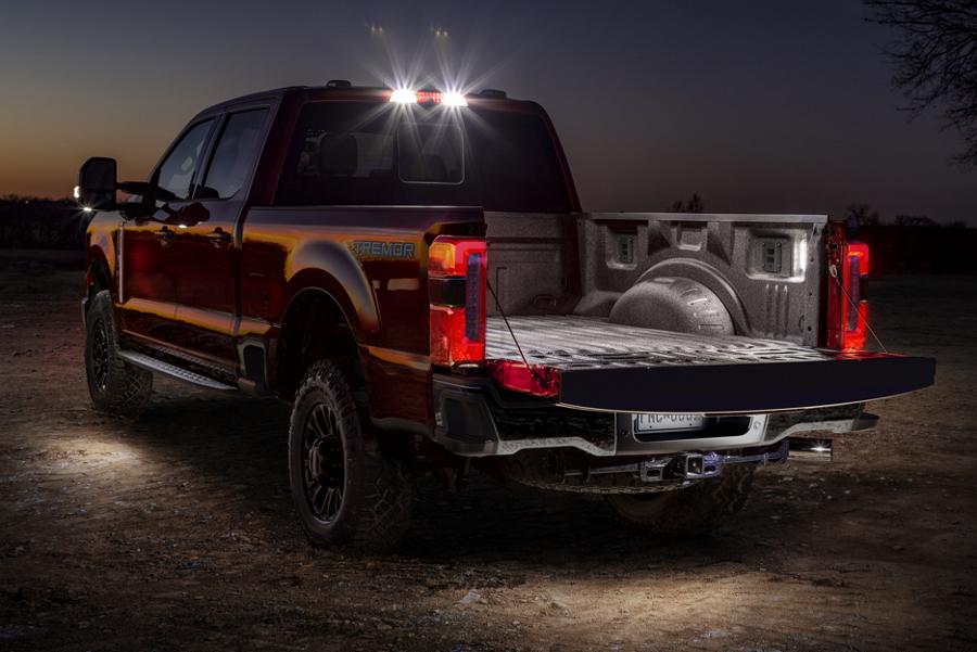 A 2025 Ford Super Duty® F-250® LARIAT® model at night with LED lights turned on in the truck bed, side mirrors and rear cab