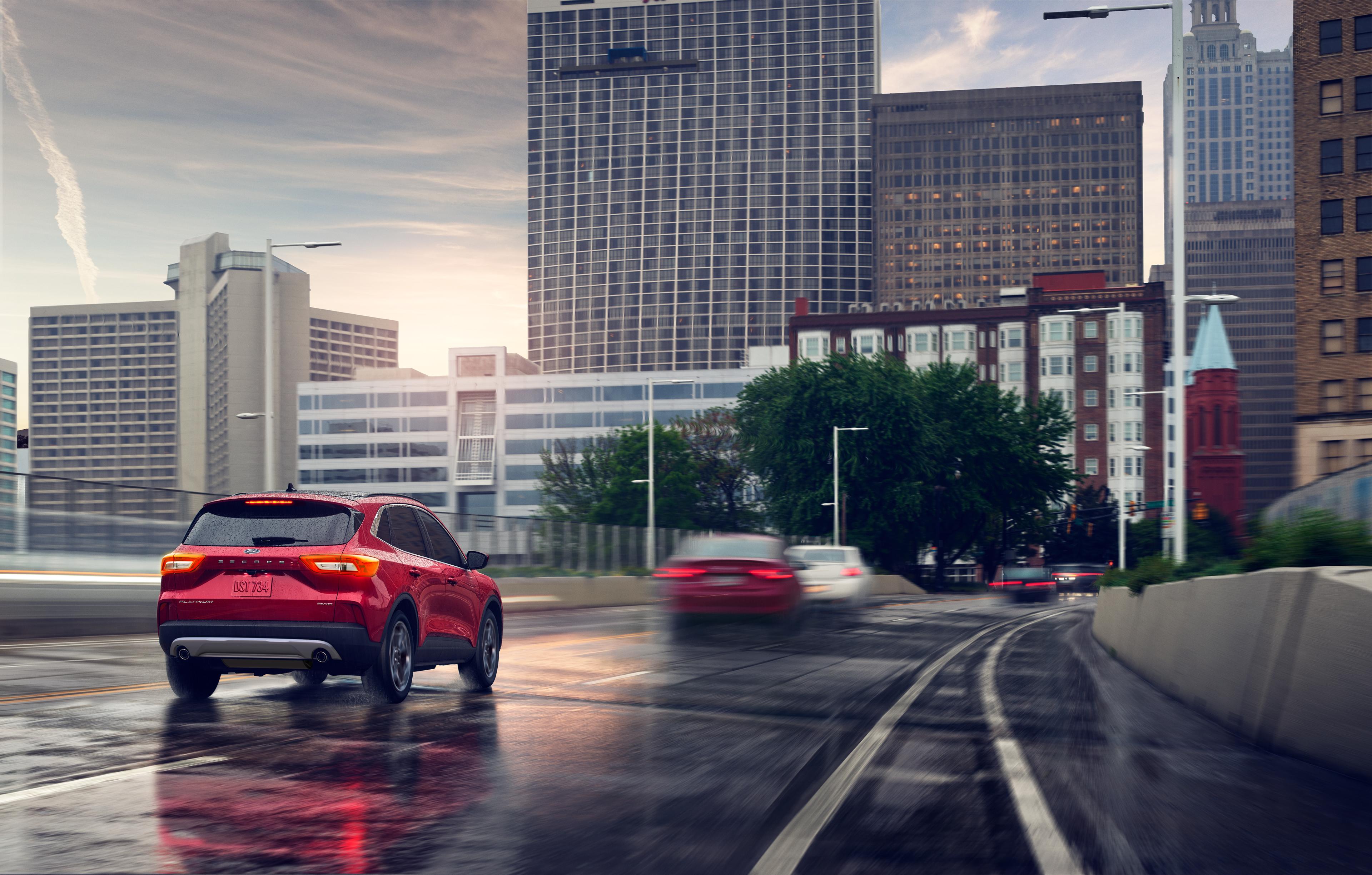 Rear view of a 2026 Ford Escape® SUV being driven on a rainy freeway toward a city skyline